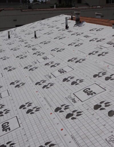 A house roof covered with GAF Tiger Paw synthetic roofing underlayment, with roof vents and pipes visible, during roofing installation.